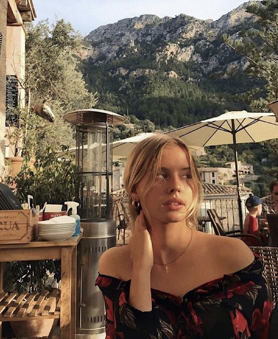 a woman sitting at an outdoor table with mountains in the backgrouf behind her