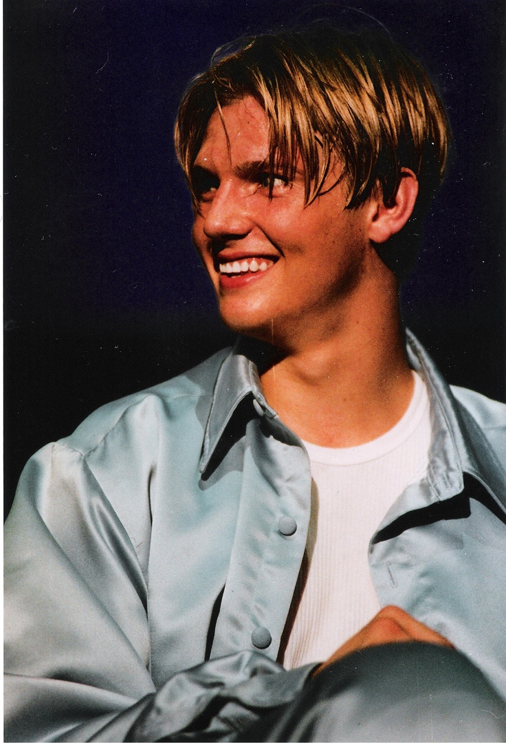 a young man with blonde hair smiling and wearing a light blue shirt over his shoulders