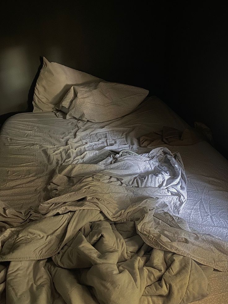 an unmade bed in a dark room with white sheets and blankets on top of it