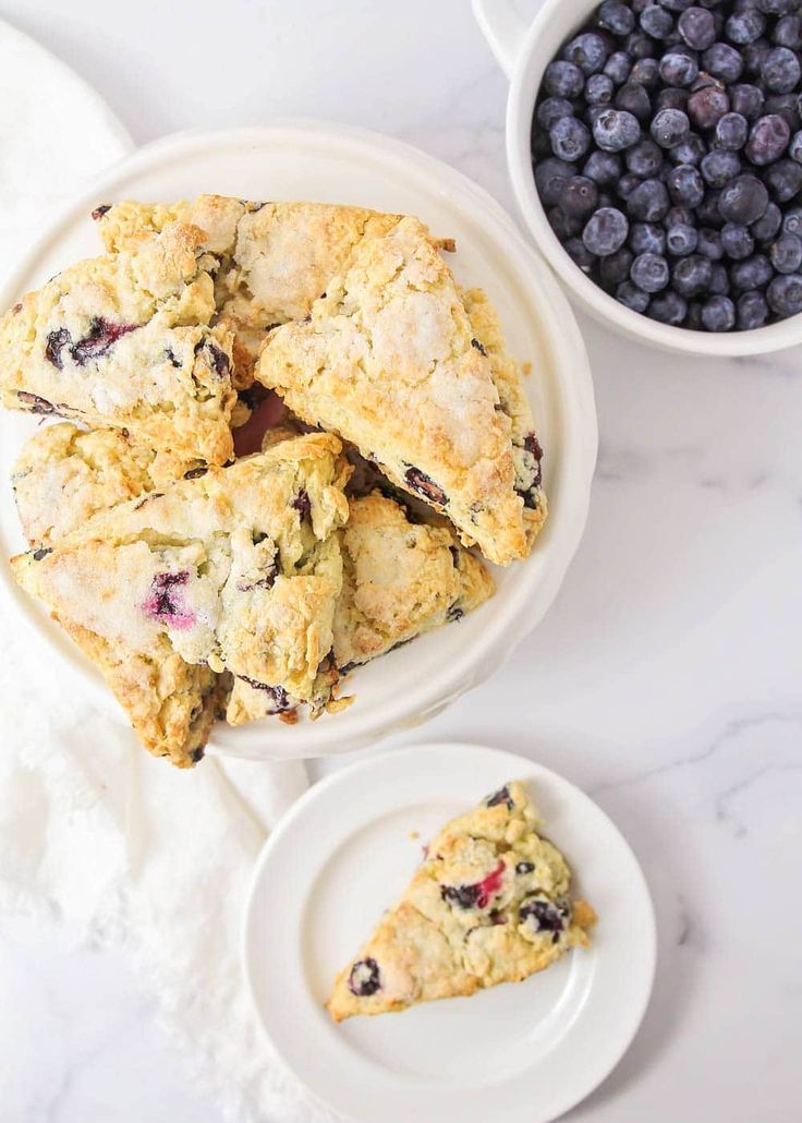 blueberry scones are sitting on plates next to a bowl of blueberries