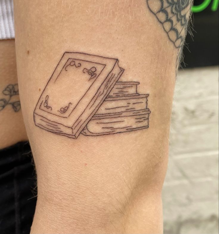 a couple of books tattoo on the arm and leg, with one book sitting on top of each other