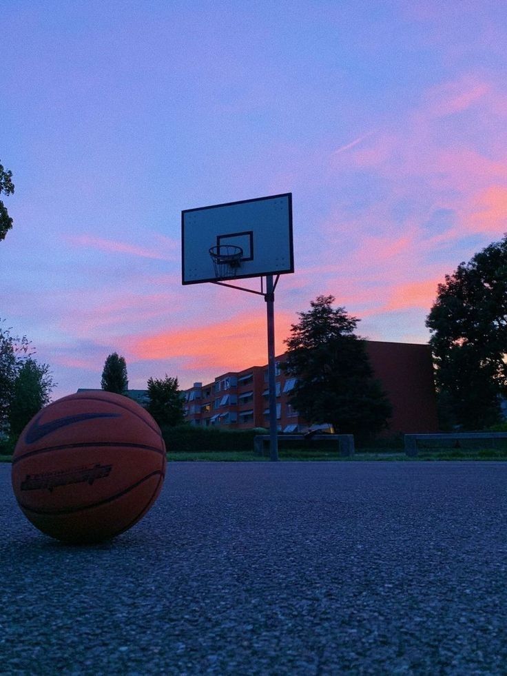 a basketball is sitting on the ground in front of a basket ball at sunset or dawn