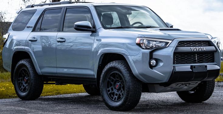 the front end of a silver toyota 4runner parked in a parking lot next to grass and trees