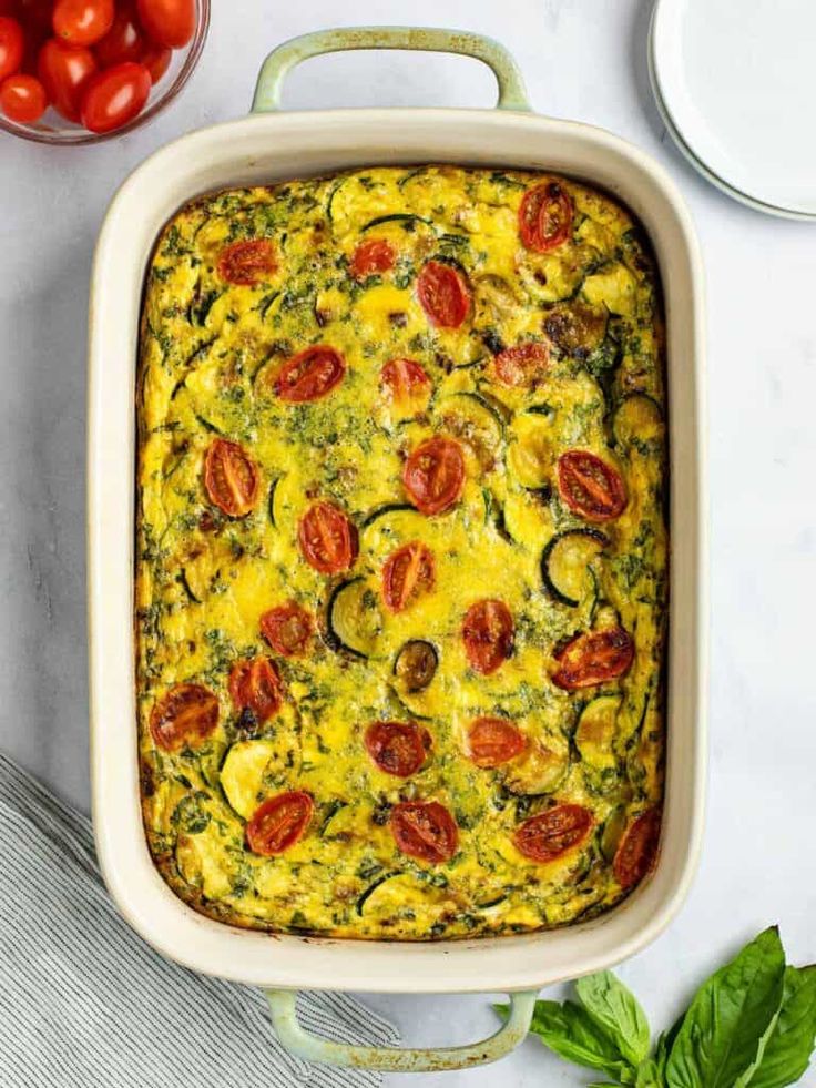 a casserole dish with tomatoes, zucchini and spinach