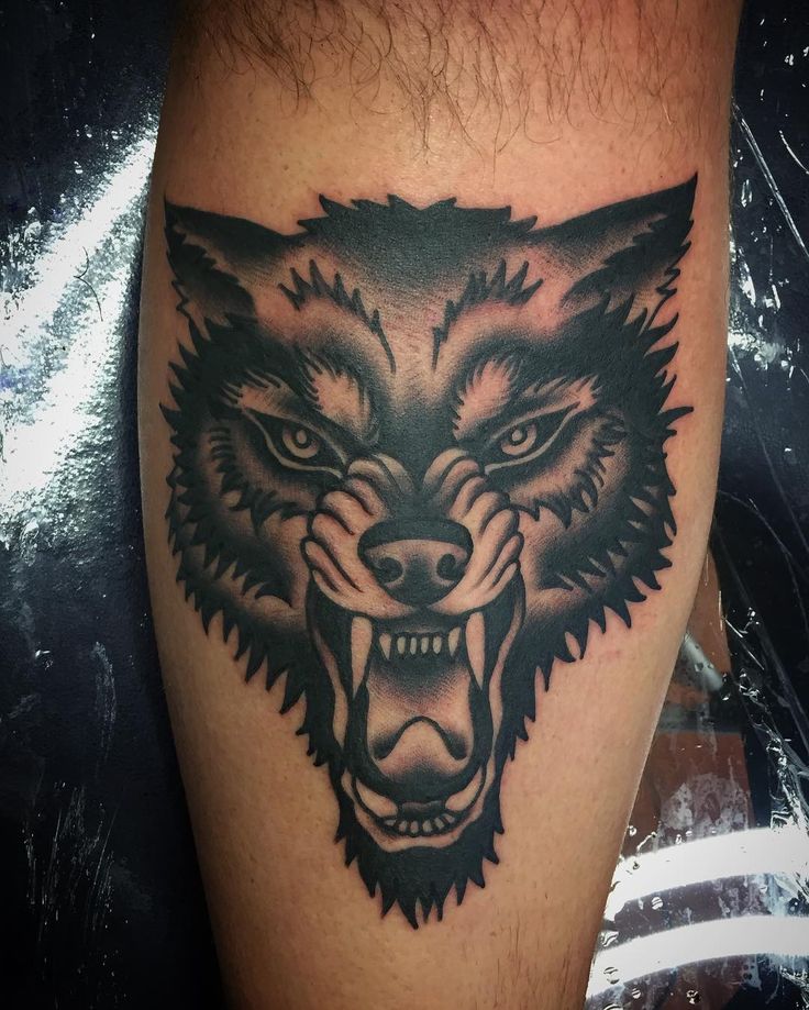 a black and grey tattoo on the leg of a man with an angry wolf head