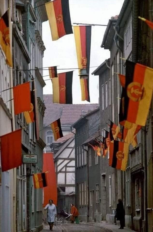 some people are walking down an alley way with flags hanging from the side of buildings