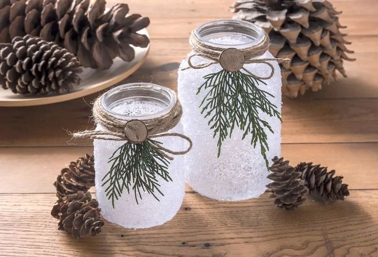 two mason jars decorated with pine cones and twine are sitting on a wooden table