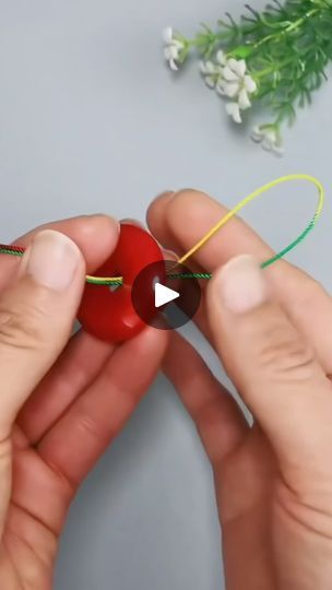 two hands are holding something red and green with a string attached to it while another person holds the string in front of them