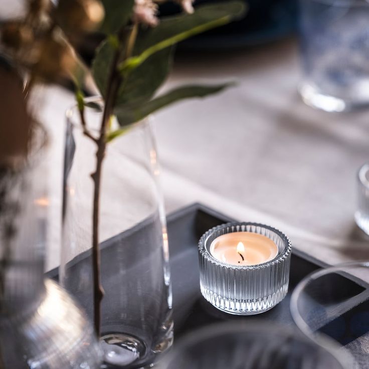 a candle is sitting on a tray next to a glass vase with flowers in it