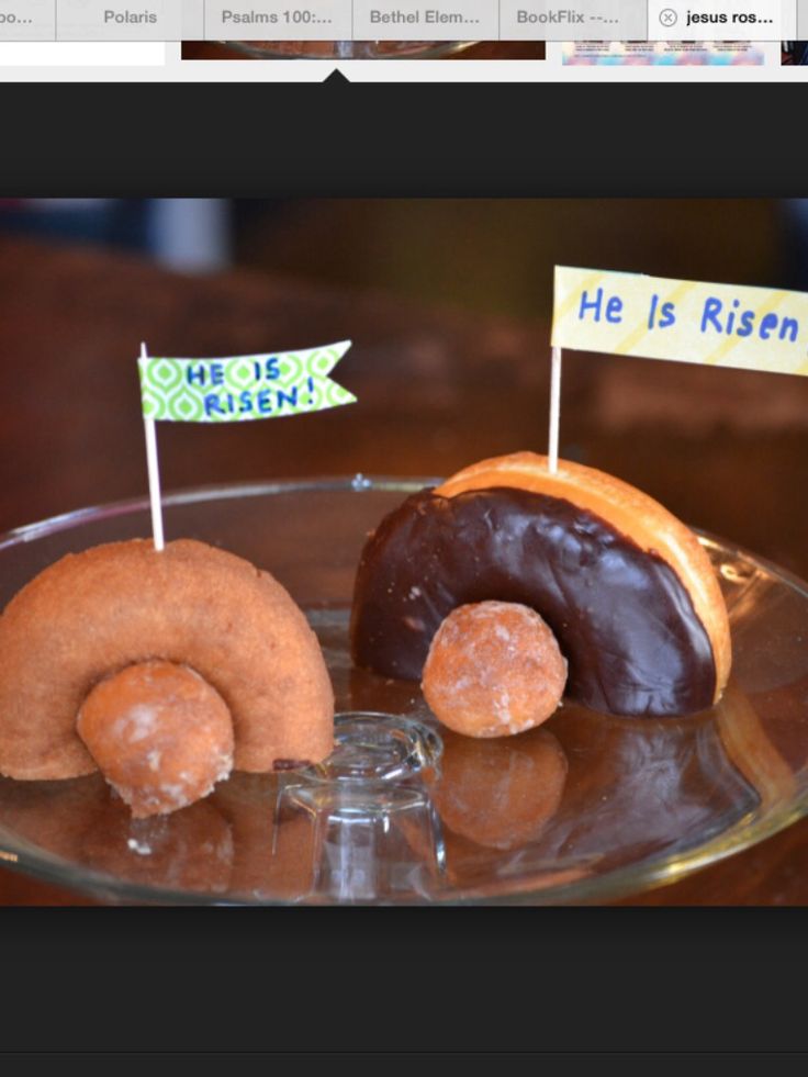 two doughnuts on a glass plate with small signs in front of them that say he is risen