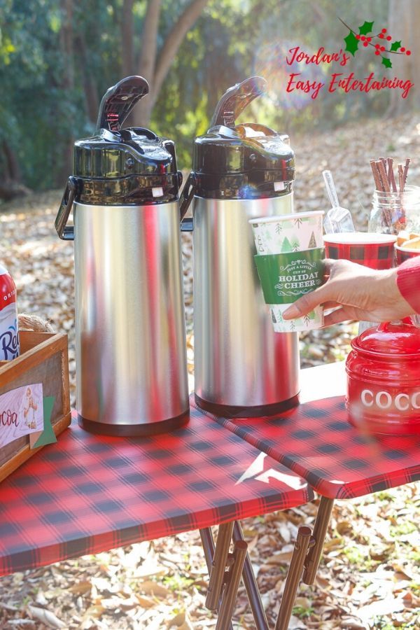 two stainless steel coffee mugs sitting on top of a red and black picnic table