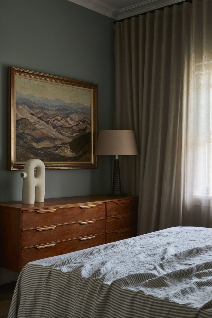 a bedroom with a painting on the wall next to a bed and dresser in front of a window