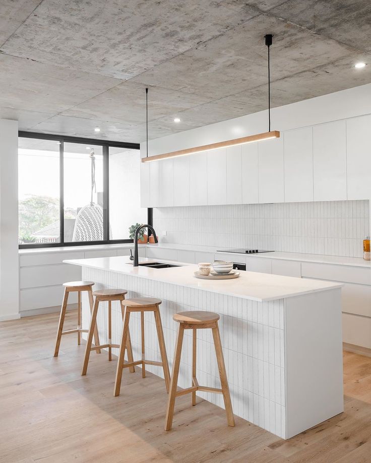 a white kitchen with three stools next to an island