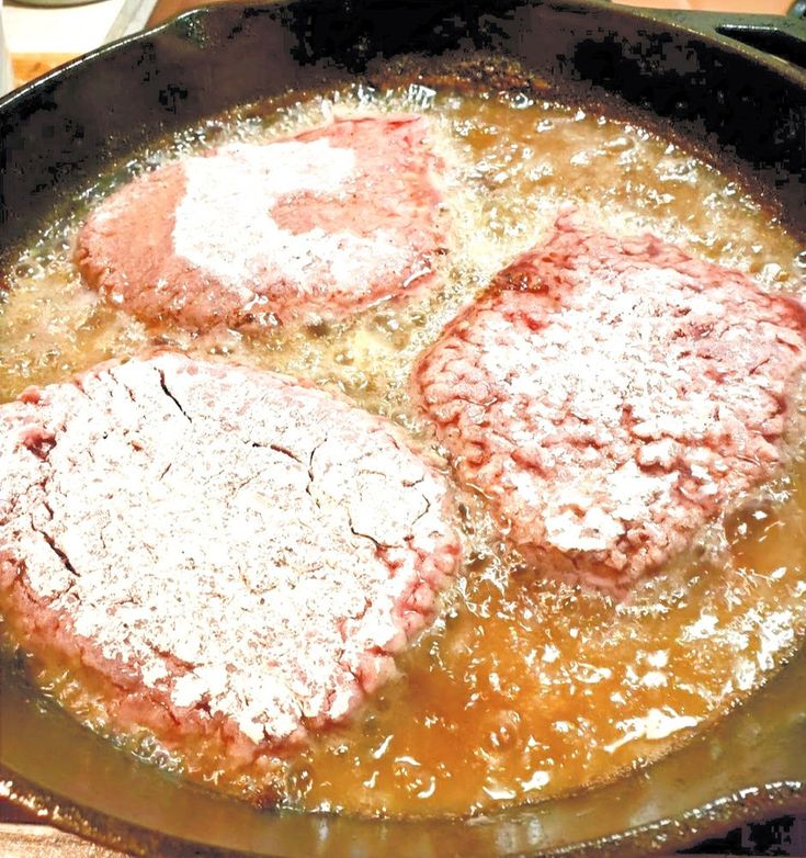 two hamburger patties cooking in a skillet