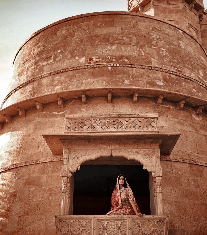 a woman is sitting on a balcony in front of an old brick building and looking out the window