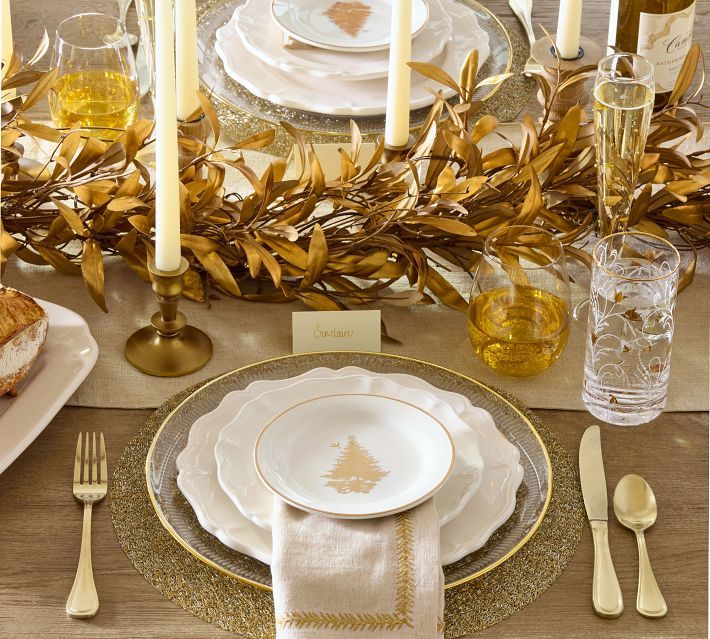 the table is set with gold and white plates, silverware, candles, and napkins