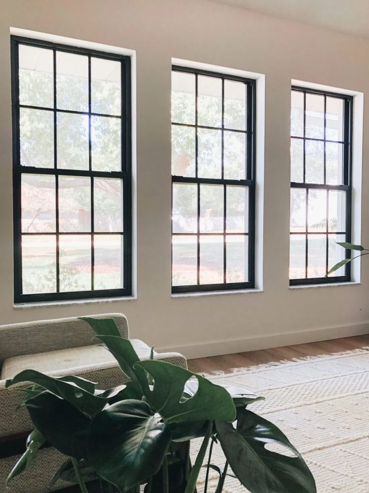 a living room with three large windows and a rug on the floor in front of it