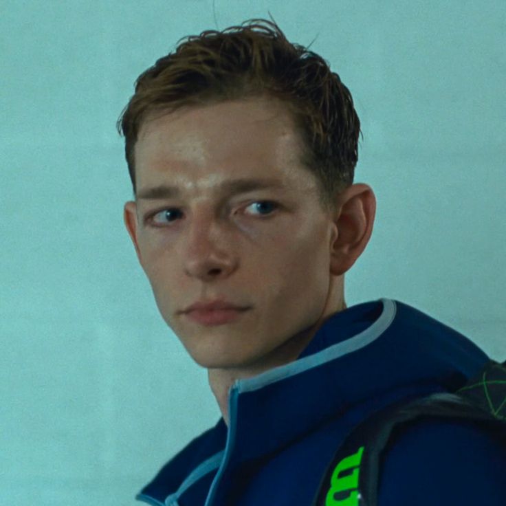 a young man wearing a blue jacket and green lettering on his chest is staring at the camera