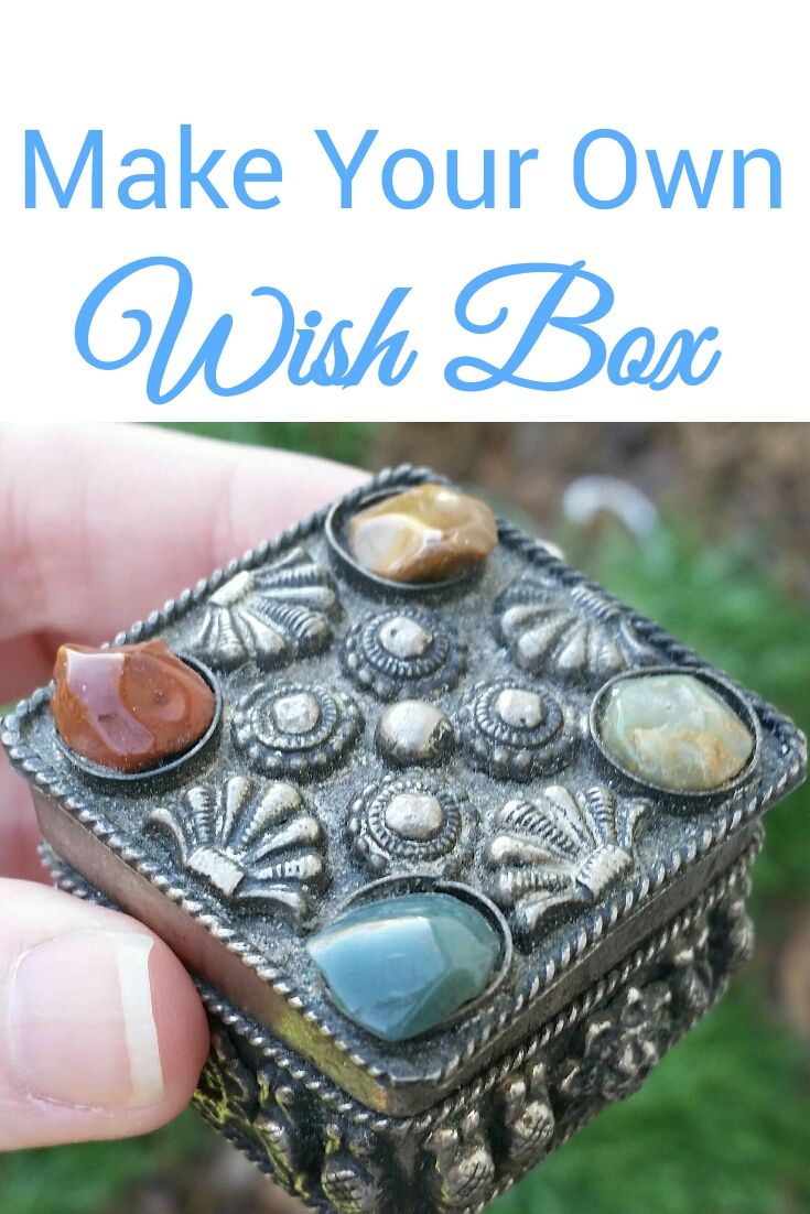 a hand holding a small metal box with stones on it and the words make your own wish box