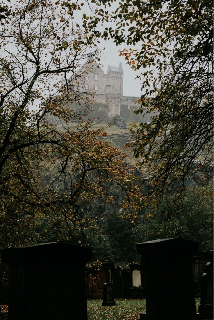 an old castle sits on top of a hill behind some tombstones in the grass