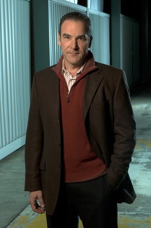 a man standing in an alley with his hands in his pockets and wearing a jacket