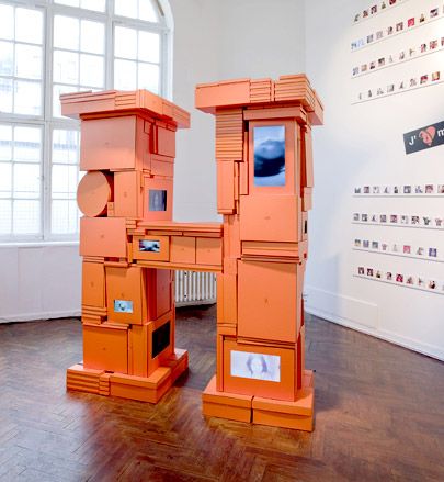 an orange sculpture sits in the middle of a room with windows and pictures on the wall