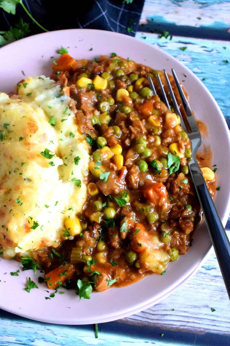 a white plate topped with mashed potatoes, peas and corn next to a fork