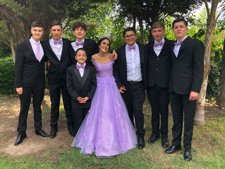 a group of young men and women in formal wear posing for a photo together outside