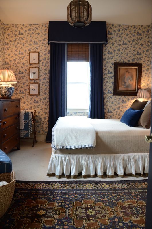 a bedroom with floral wallpaper and blue drapes on the window sill, along with a large bed