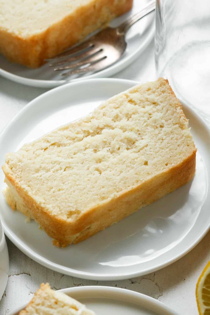 two slices of cake on white plates with silverware and lemons in the background