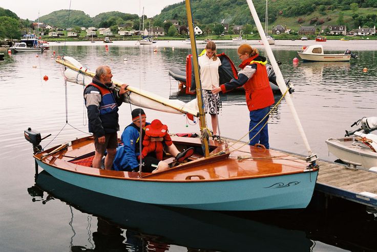 several people in life jackets standing on a small sailboat at the dock with other boats