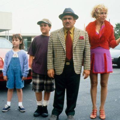 a group of people standing next to each other in front of a red car on the street