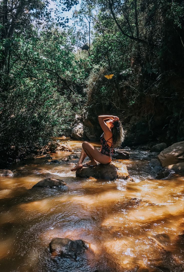 a woman in a bathing suit sitting on rocks next to a river with brown water