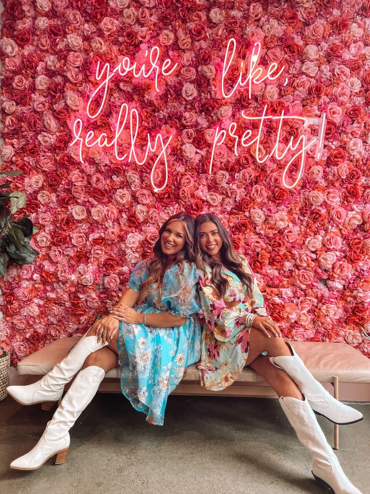 two women sitting on a bench in front of a flower wall with the words you're like really pretty