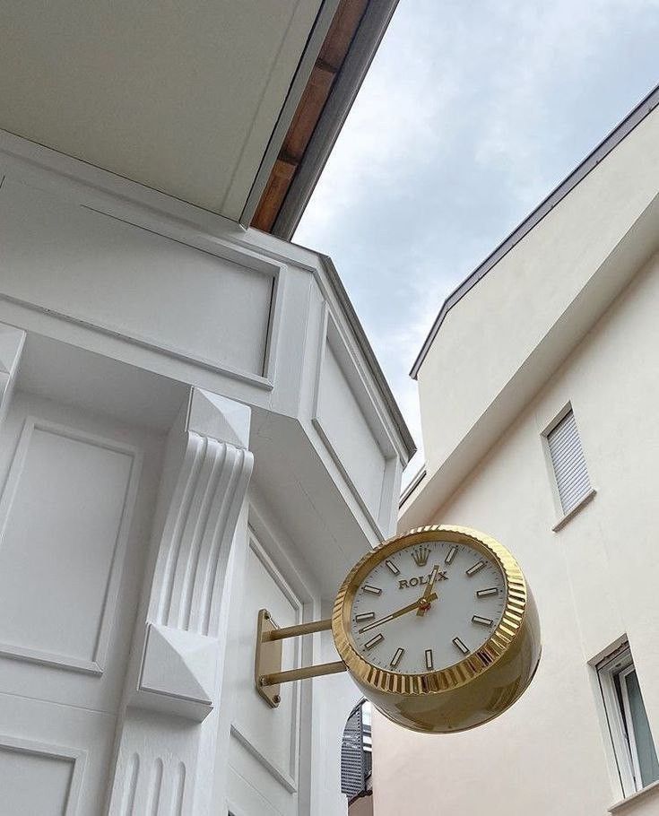 a clock hanging from the side of a white building next to a tall wall with windows