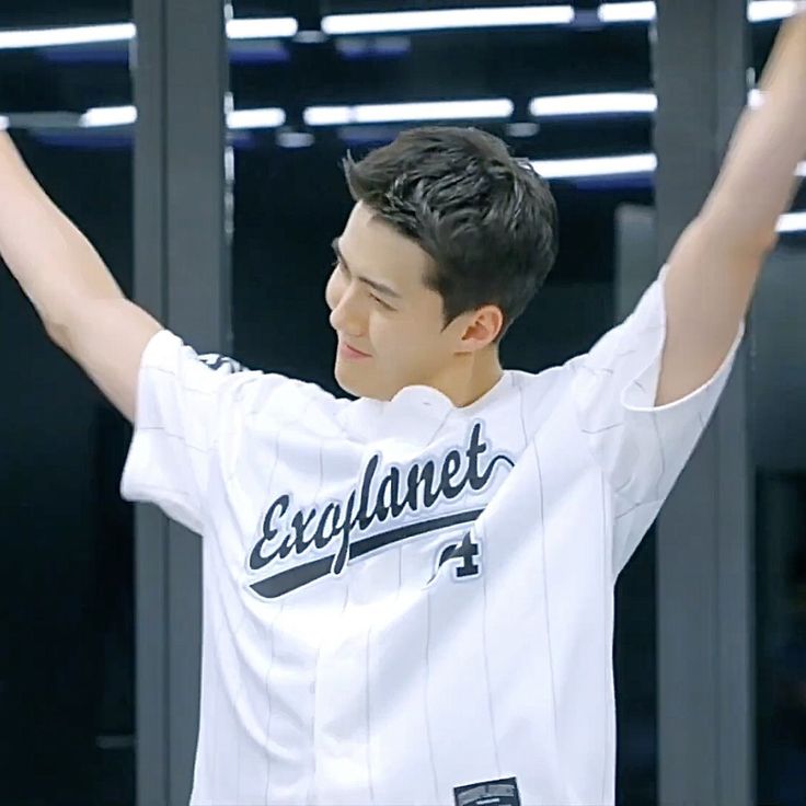 a young man holding his arms up in the air while wearing a white shirt with black lettering on it