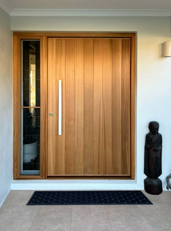 the front door is made of wood and has a black mat on the floor next to it