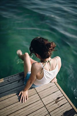 a woman sitting on a dock looking at the water