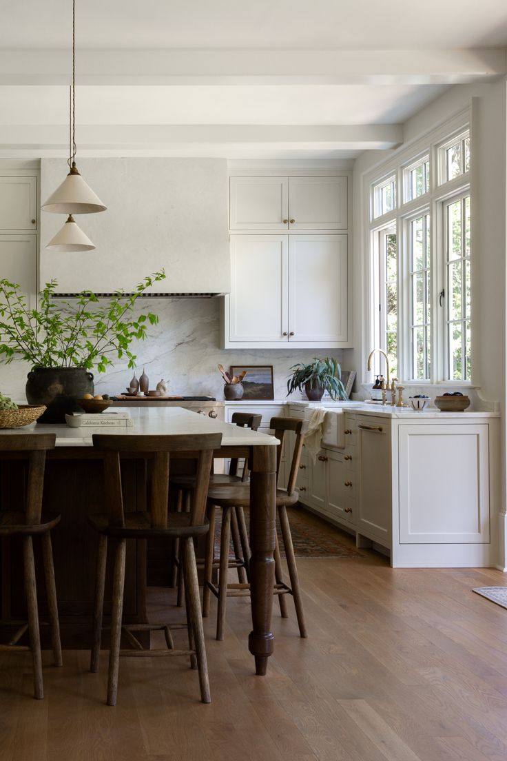 a kitchen with white cabinets and wooden floors, an island table surrounded by chairs in the center