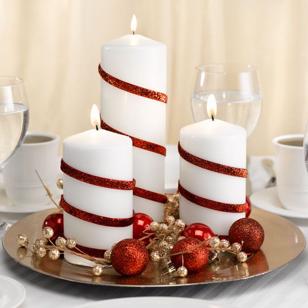 three white candles sitting on top of a plate with red ribbon around them and christmas decorations