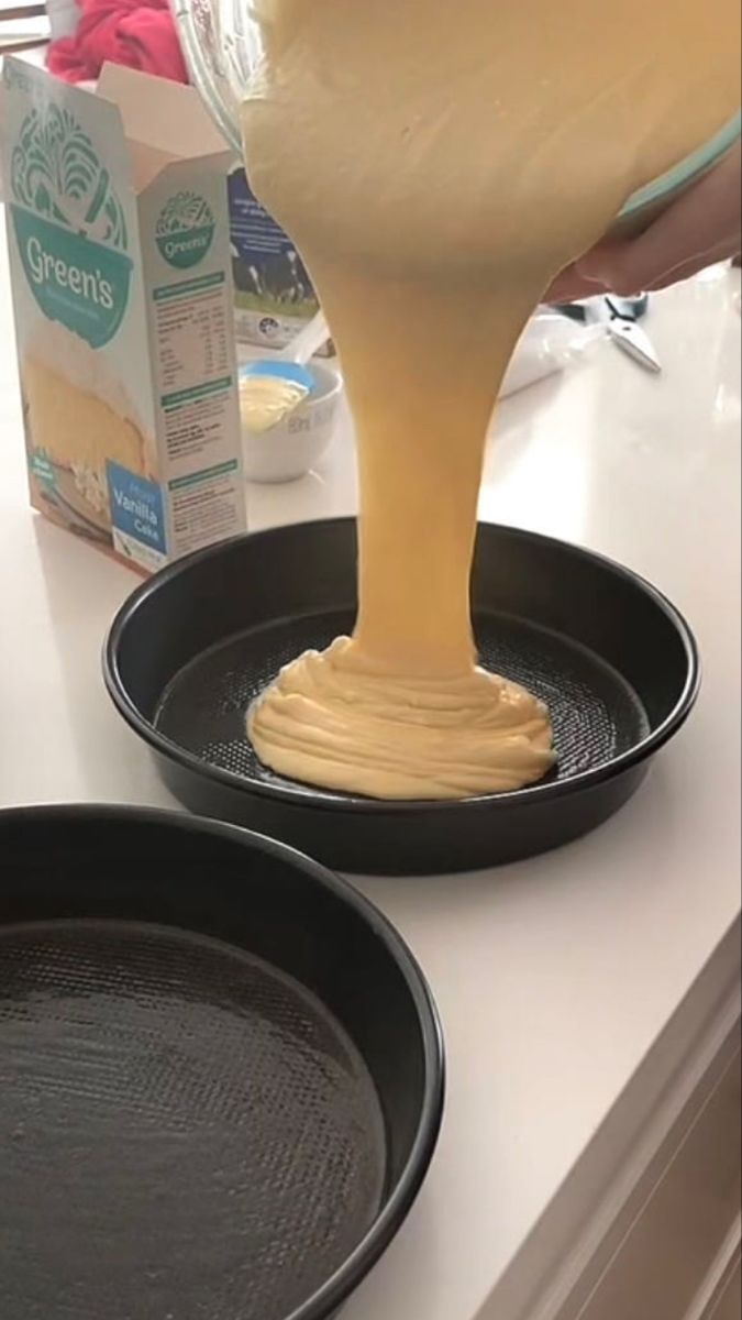 a person pouring batter into two black pans on top of a counter next to a carton of milk