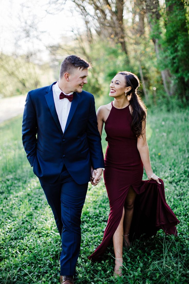 a man and woman in formal wear walking through the grass