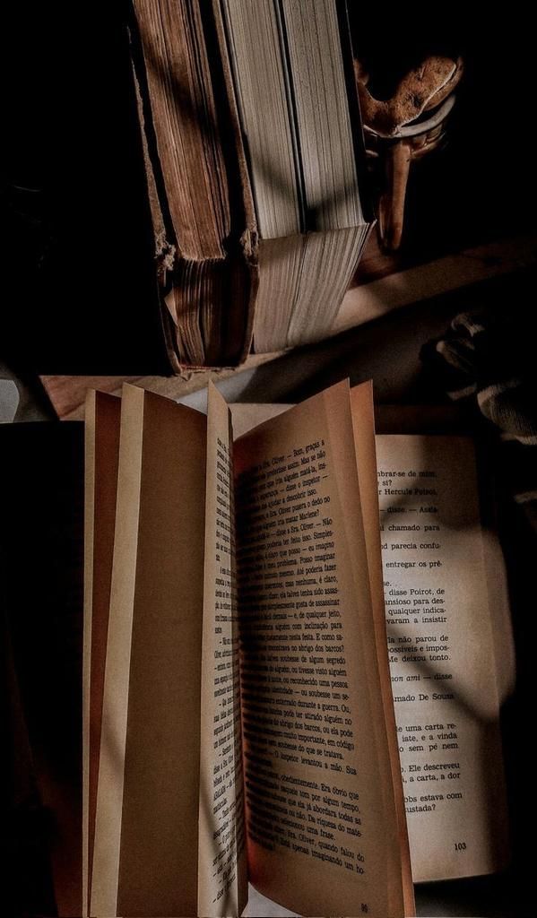 an open book sitting on top of a wooden table next to a pile of books