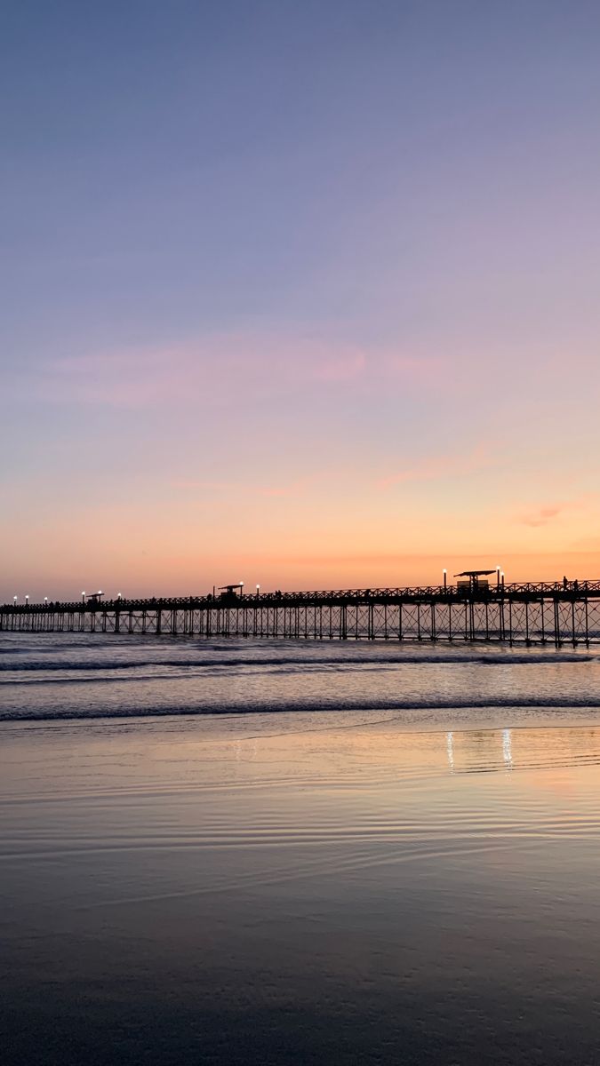 the sun is setting over the ocean and a long pier stretches out into the distance