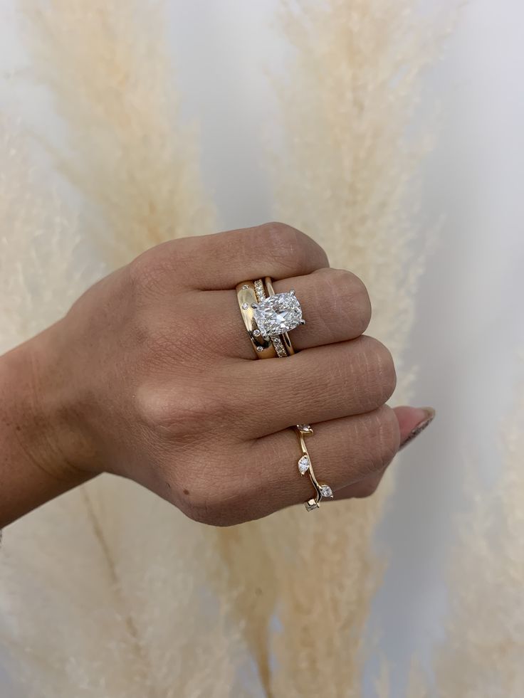 a woman's hand with two rings on it and some flowers in the background