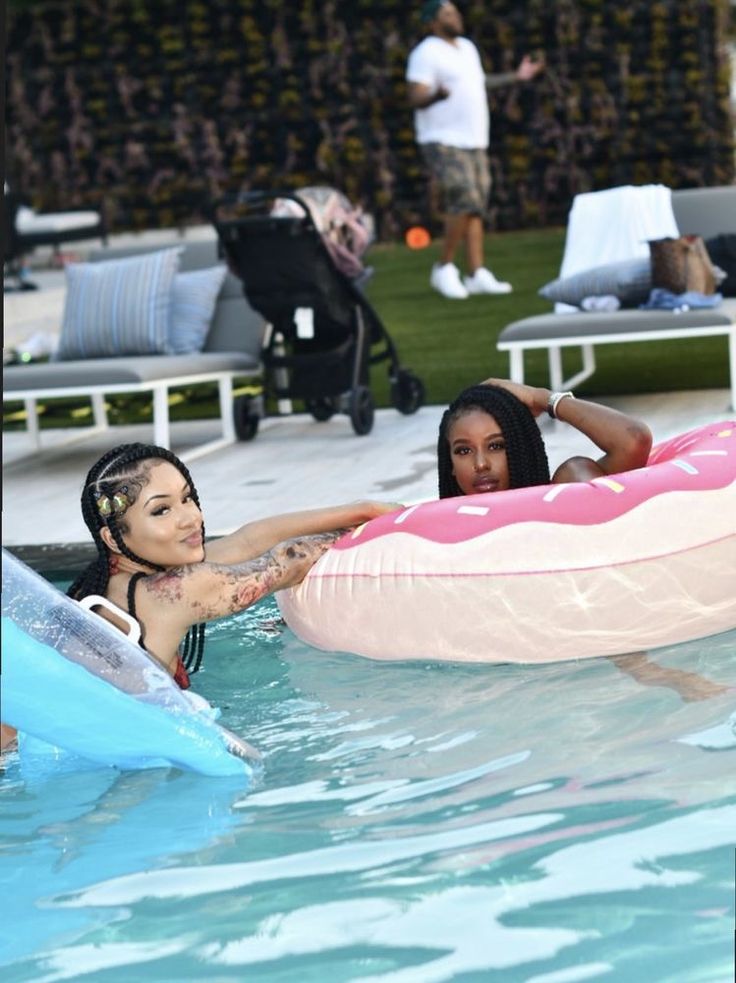 two women are in the pool and one is holding an inflatable pink float