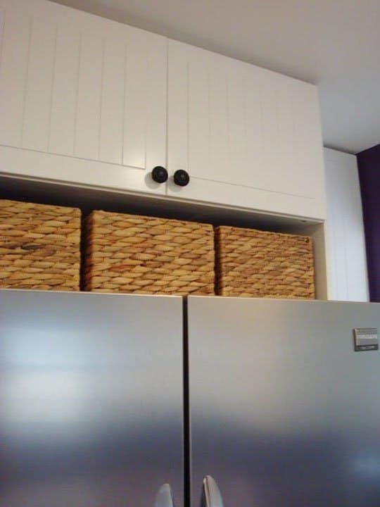 two stainless steel refrigerators with wicker baskets on the top and bottom, in front of white cabinets