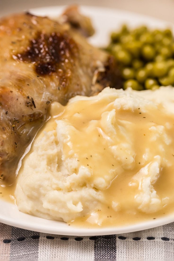 a white plate topped with mashed potatoes and green peas next to meat covered in gravy