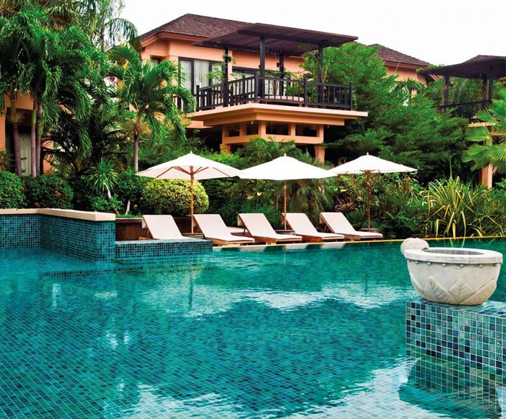 an outdoor swimming pool with lounge chairs and umbrellas in front of the resort building