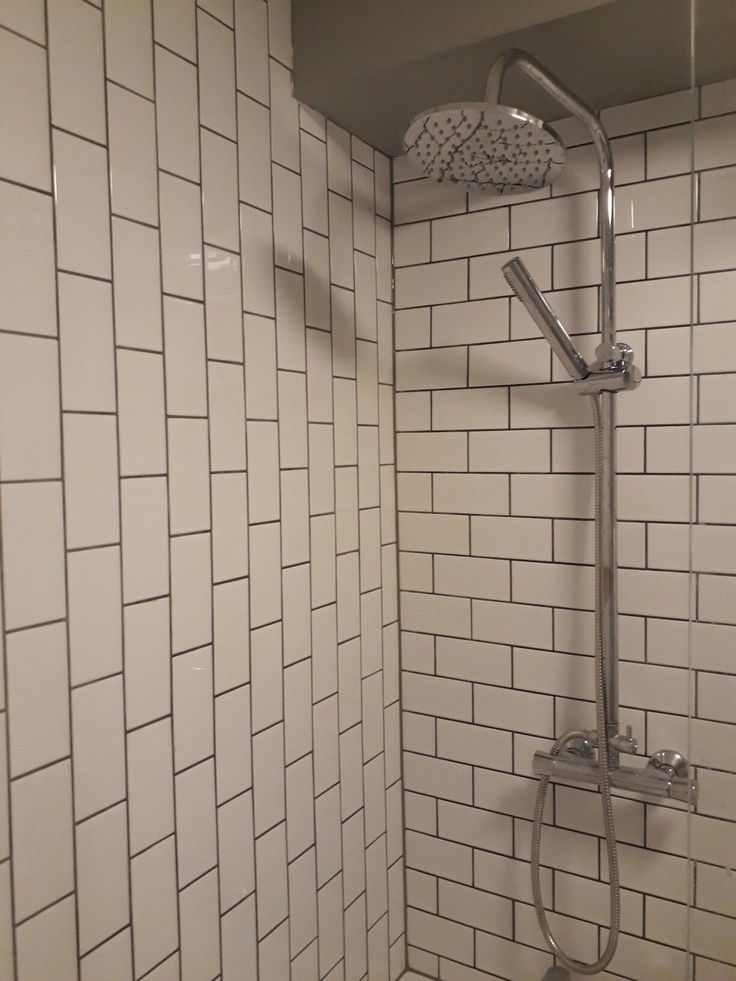 a shower head and hand rail in a white tiled bathroom with grey grouting